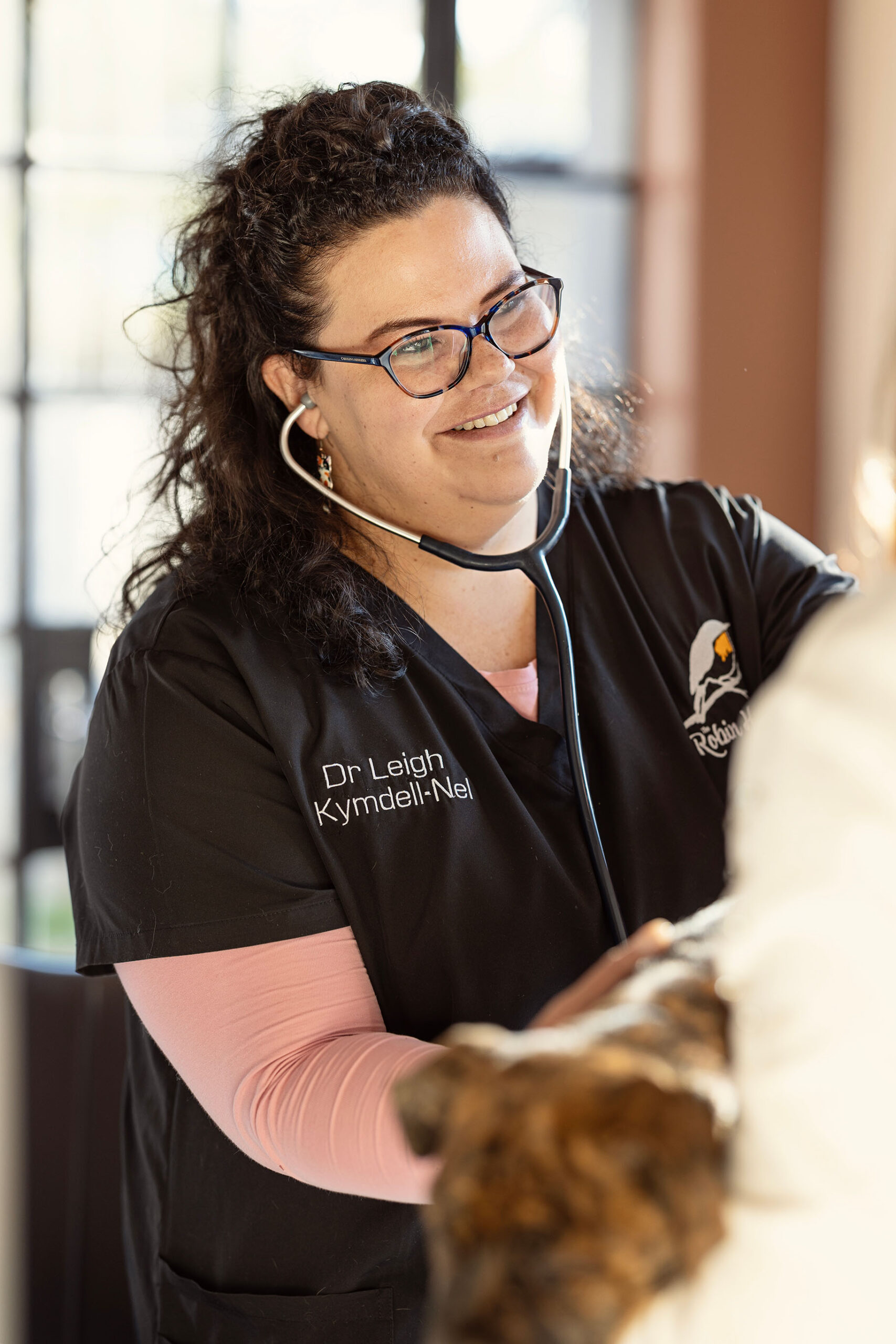 Dr. Leigh Kymdell-Nel smiling while using a stethoscope to examine a brindle dog at The Robin House veterinary practice in Benoni.