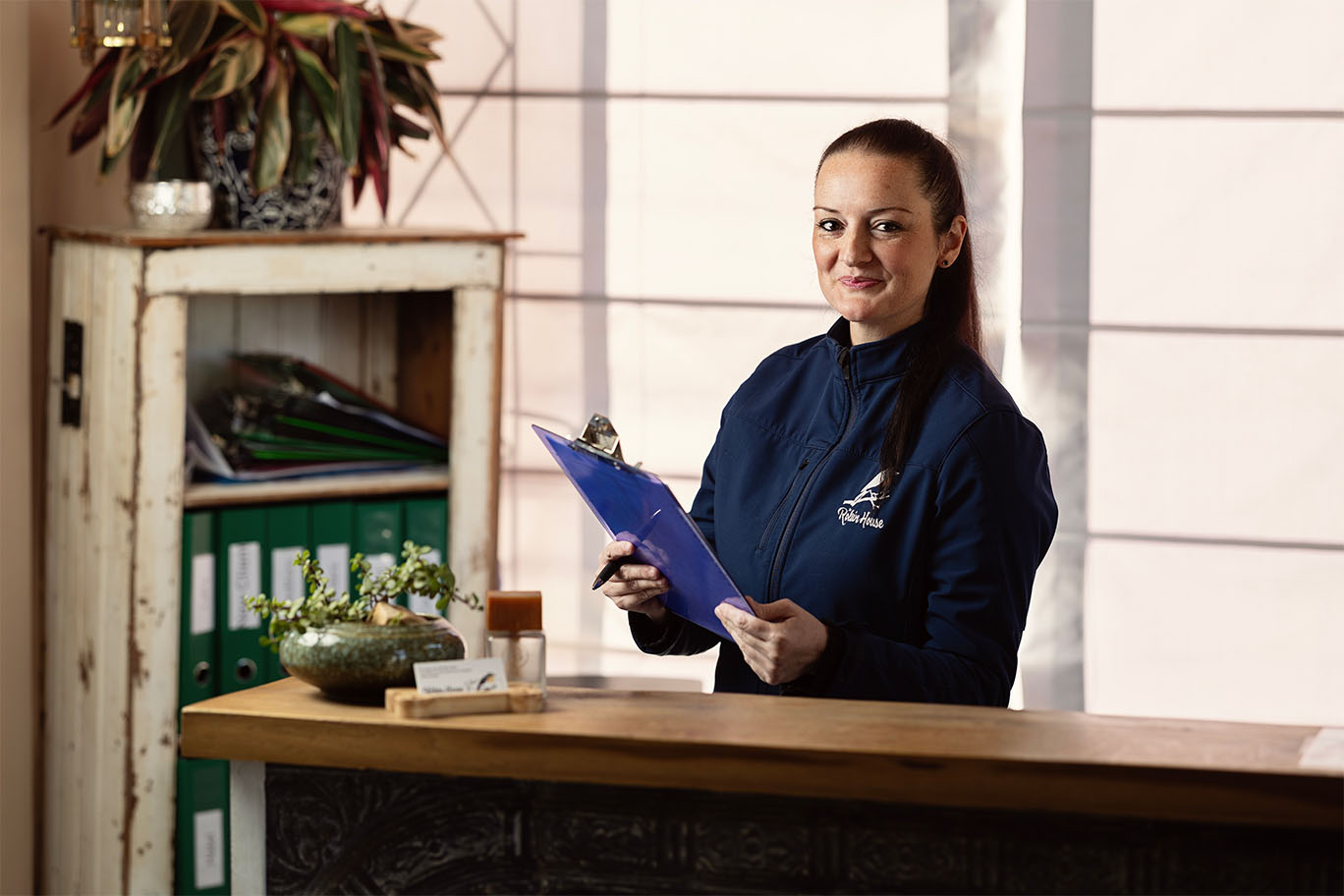 A friendly receptionist at the front desk of The Robin House veterinary hospital in Benoni holding a blue clipboard.